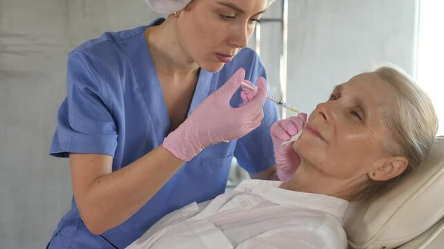 Elderly woman undergoing lips augmentation and lift procedure in cosmetology clinic. Qualified female cosmetologist injecting fillers to improve lip proportions to patient