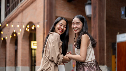 Obraz premium Two beautiful Asian female friends enjoy shopping together in the city, smiling at the camera.