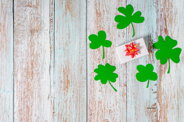 Green four leaf clovers and giftbox on white wooden background top view. Happy St. Patrick's Day greetings