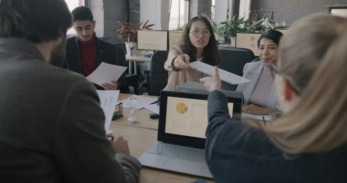 Businesswoman team leader handing out documents talking to employees at meeting in office. Professional gathering and workplace concept.