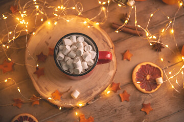 Cute cozy winter composition. red mug, marshmallows, oranges and Christmas lights.