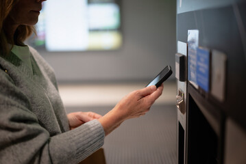 Close-up of a woman driver standing in front of a parking machine and paying with smartphone