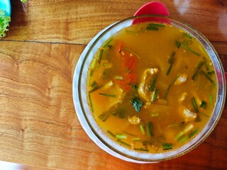 Thai spicy soup with fish and vegetables in a bowl on wooden table