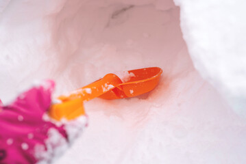 Close-up of a child's hand holding a plastic shovel and dripping snow with it. Winter fun, leisure. Hello winter