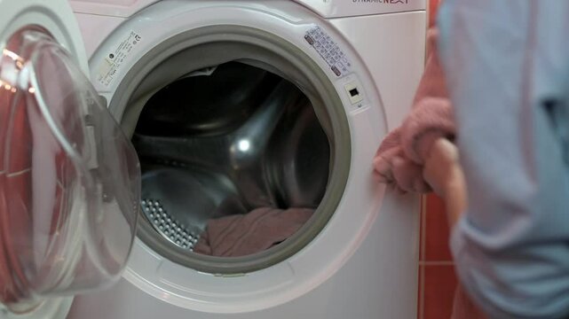 Close-up of person loading pink towel into front-loading washing machine, emphasizing laundry day chores and household activities. person loading into washing machine, loading into washing machine