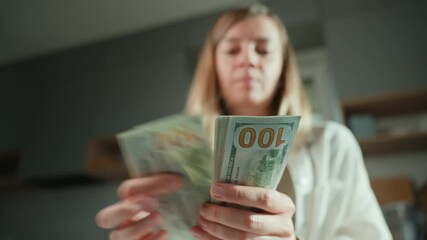 Woman counting stack of dollar bills at home. Female holding american dollars cash. Concept of cash management, wealth or financial transactions