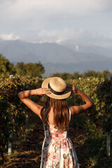 An Elegant Woman in a Floral Dress Stands Gracefully Against a Scenic Vineyard Landscape