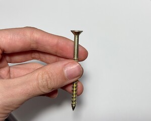 A man holds a screw in his hand, a bolt on a light background. Devices for repairing and mending...