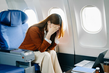 Photo of a frustrated woman sitting on an airplane with her head in her hands