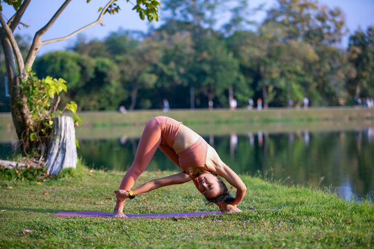 Young woman practicing yoga on soft green grass beside the lake. Young woman practicing yoga in nature. Healthy lifestyle. Concept of vitality, balance, mindfulness, Zen energy, calmness, relaxation, 