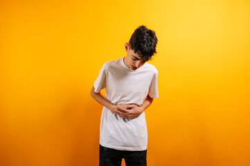 Teenager clutching stomach, pain, discomfort, yellow background.