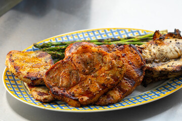 Grilled meat, chicken and pork and grilled green asparagus on a blue and yellow plate