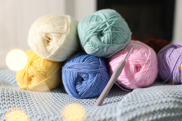 Many colorful yarns and crochet hook on blanket among blurred lights, closeup