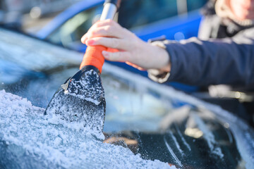 Woman deicing car windshield with ice scraper