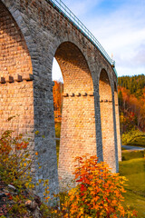 On a sunny autumn day, the railway viaduct in Smrzovka showcases stunning stone arches surrounded...