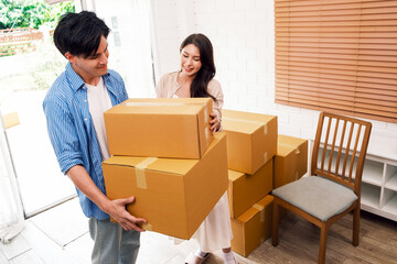 Asian young happy new married couple moving to their new house or real estate. An attractive romantic man and woman carry boxes parcel with happiness and love. Family moving house relocation concept.