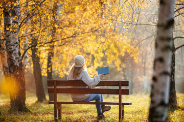 Woman is relaxing in autumn park and reading book to improve her mindfulness and mental wellbeing....