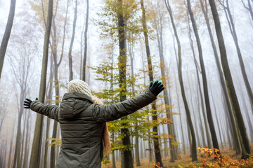 Forest bathing. Woman is enjoying walk in autumn foggy woodland. Mental wellbeing and mindfulness...