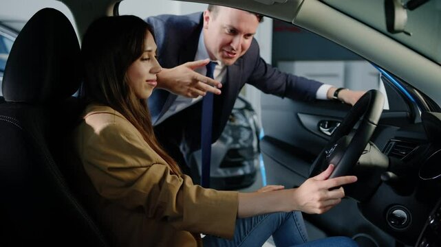 The male manager tells the young woman the new features of the car. Buyer in the showroom