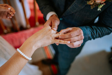 Close-up of a groom placing a wedding ring on the bride’s finger during a ceremony, symbolizing their commitment and love..