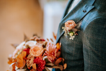 A groom’s suit adorned with a peach rose boutonniere, holding a bouquet of vibrant flowers, creating a stylish and romantic wedding detail..