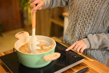 Young woman in sweaters cooking spaghetti in a cozy kitchen. People, food and domestic life concept