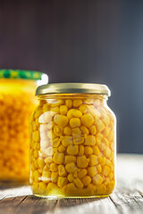 Canned sweet corn in jar on wooden table.