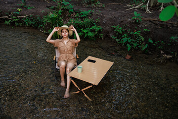 woman sitting on a chair in the stream flowing and drinking coffee  in her hand, relaxtion in holiday concept.
