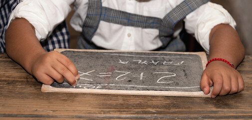Old vintage historic school with wooden brown tables, with pupils in the class. Child write on the blackboard with chalk