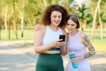 Two women share laughter while looking at a phone in a vibrant park.