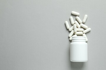 Various medicines and health pills poured from a medical white bottle, healthcare and medical top view on a gary background.
