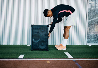 Fit young man in sportswear connecting his smart phone to a large wireless speaker to play some music before a gym workout session