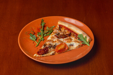 Slice of Italian pizza with cherry tomatoes and meat on a plate on a wooden background