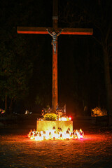 Wooden cross adorned with jesus christ statue illuminated by numerous candles and flowers in a...
