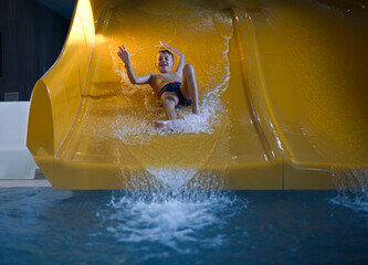 Boy having fun sliding down waterslide into pool, enjoying summer vacation at aquapark