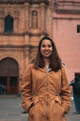 Young woman in a brown coat with fur trim walks along a stone wall in an urban setting.0