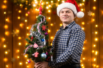 A man poses with christmas tree toy in New Year decorations with festive illumination and garlands, Christmas lights and decorations background, Holiday theme