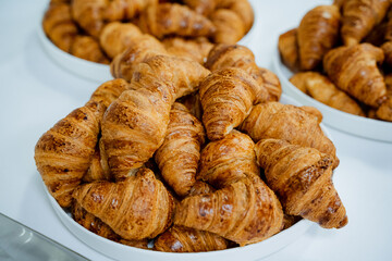 Three charming bowls of flaky croissants are artistically arranged on a beautifully crafted wooden table, emitting a golden aroma that entices everyone to indulge in their delightful taste