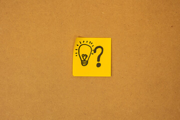 Yellow paper with a drawing of a light bulb shining and a question mark, concept of ideas