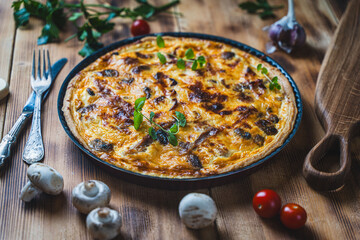 Quiche or pie with meat, chicken and mushrooms on a wooden table with cutlery, herbs and cherry tomatoes