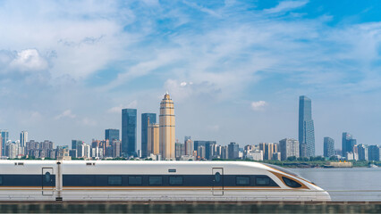 Naklejka premium Modern High-Speed Train Passes by Urban Skyline Under Blue Sky