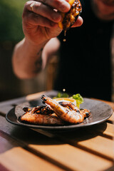 Close up focused shot of a person squeezing lemon on a grilled prawn meat in a plate on a wooden table 