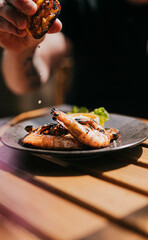 Close up focused shot of a person squeezing lemon on a grilled prawn meat in a plate on a wooden table 