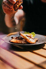Close up focused shot of a person squeezing lemon on a grilled prawn meat in a plate on a wooden table 