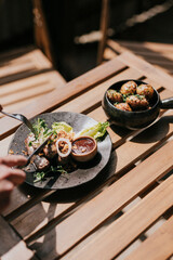A plate with some food and a person's hands with a fork and a knife on the table 