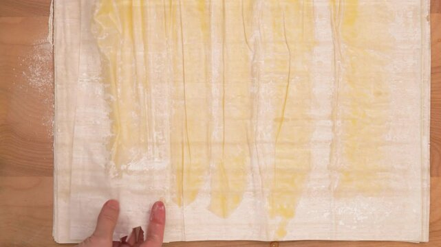 Chef folding buttered layers of phyllo dough into rolls, baking process, woman hands