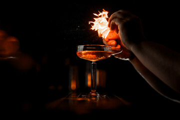 Stemmed glass with cocktail over which male hands start flame
