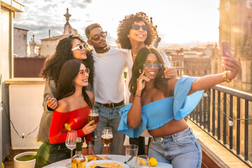 Happy multi-ethnic friends taking selfie during sunset in a rooftop