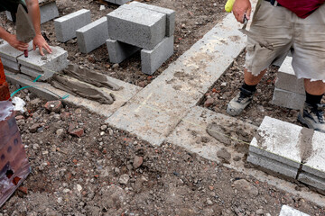 Construction workers laying gray concrete blocks for a building foundation at a job site on a sunny day in late summer