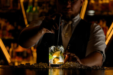 Bartender prepares a delicious cocktail with lemon wedges and mint leaves, mixing ingredients with a portable mixer